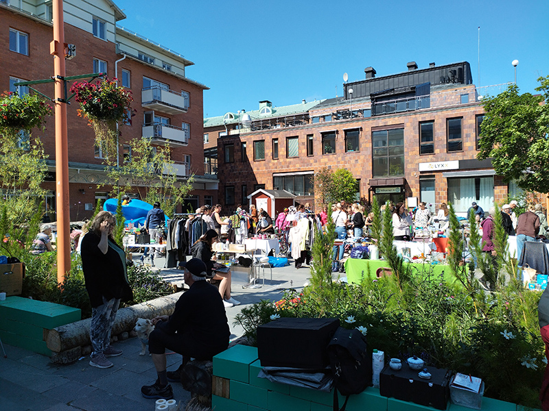 Torget är fullt av bord där folk säljer saker. Människor strövar förbi och tittar efter fynd i solskenet