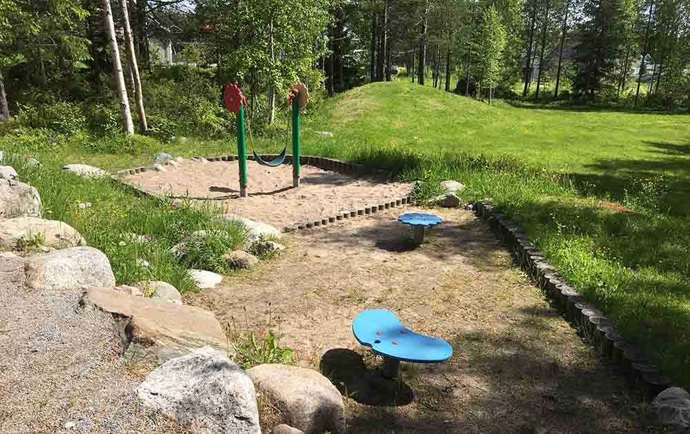 Lekgunga som hänger mellan två gröna stolpar med blommor högst upp. Två blåmålade lek- och balansleksaker framför