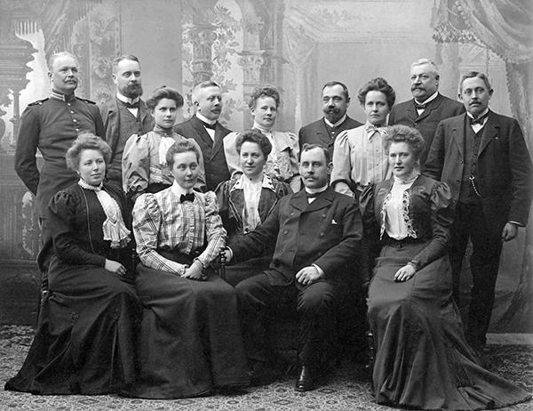 Gruppbild. Män och kvinnor, nio stående och fem sittande.