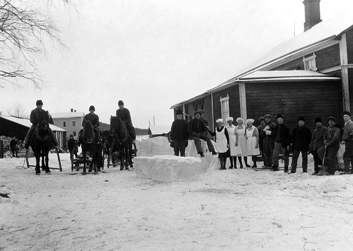 Män och kvinnor samlade kring stora isblock utanför mejeri på vintern.