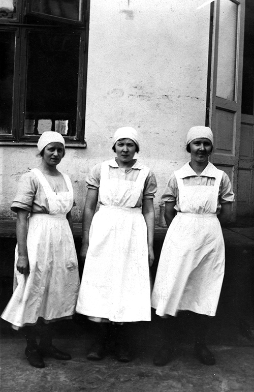 Tre kvinnor med vita förkläden och mössor.