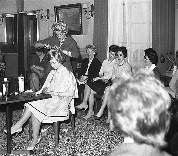 Kvinna blir klippt av frisörska medan flera kvinnor sitter och tittar på.