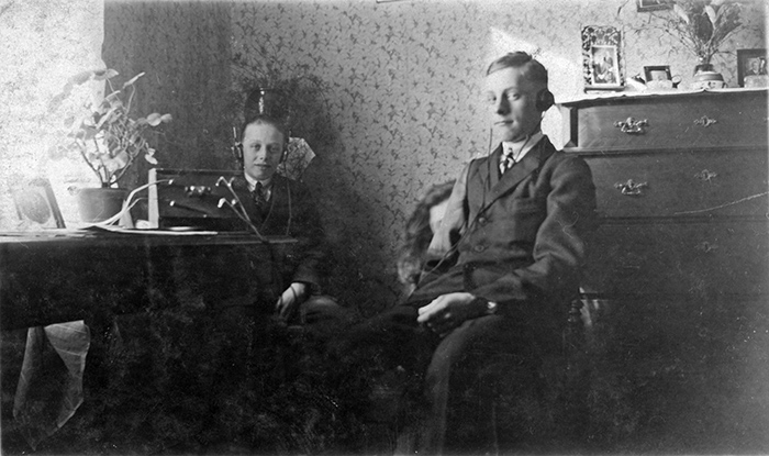 Två pojkar i kostym sittande med hörlurar i ett rum. 