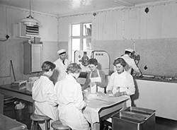 Kvinnor i vita rockar sitter vid bord och gör glassar.