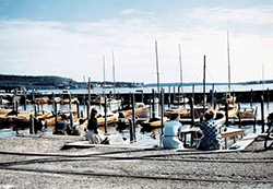 Kvinnor sitter på brygga vid småbåtshamn full av båtar.