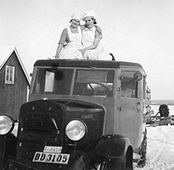 Två unga kvinnor på taket till en bil av äldre modell.