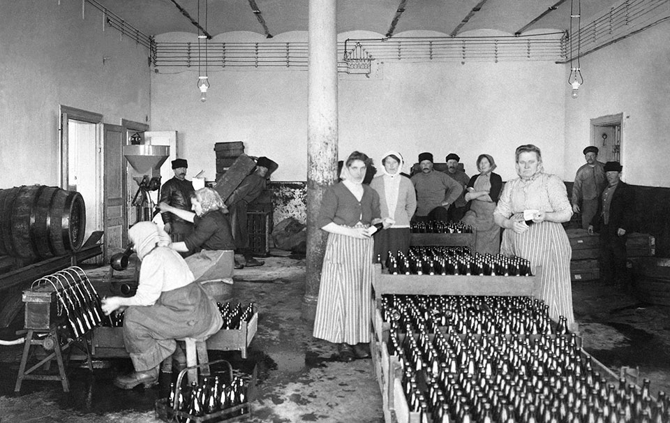 Interiör från bryggeri, många flaskor. En kvinna sitter och fyller på flaskor.