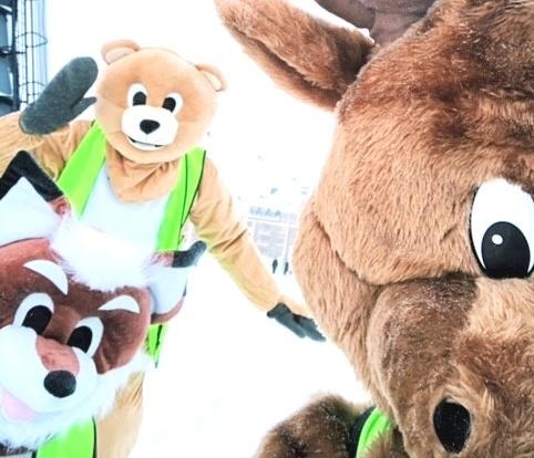 Bilden visar tre personer utklädda till maskots i form av en räv, en björn och en älg. Bilden är tagen ute på vintern.