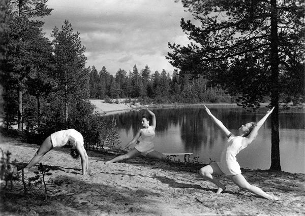 Tre kvinnliga gymnaster framför skogstjärn.