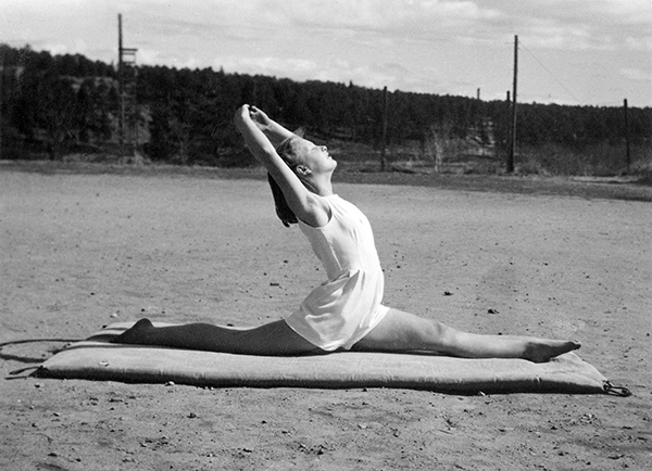 Ung kvinnlig gymnast i spagat på grusplan.