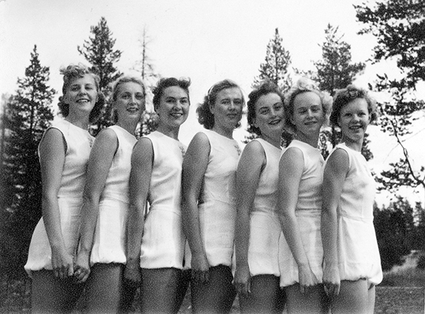 Sju kvinnliga gymnaster i vita linnen och shorts.