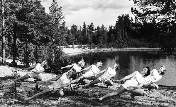 Sju kvinnliga gymnaster framför skogstjärn.