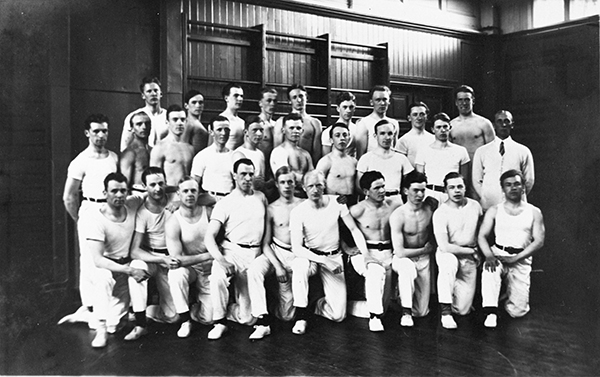 Grupp manliga gymnaster i vita gymnastikkläder.