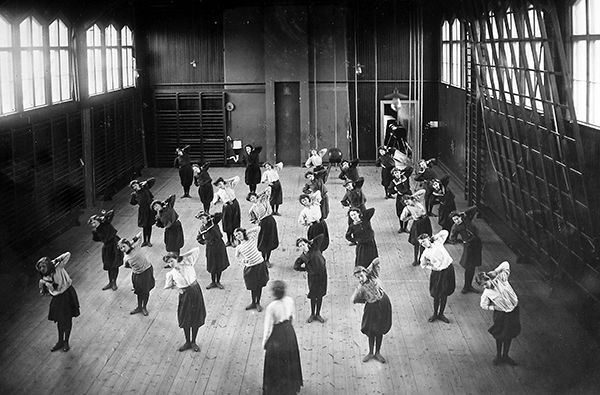 Gymnastiksal med flickor som står på golvet och böjer kroppen åt sidan.