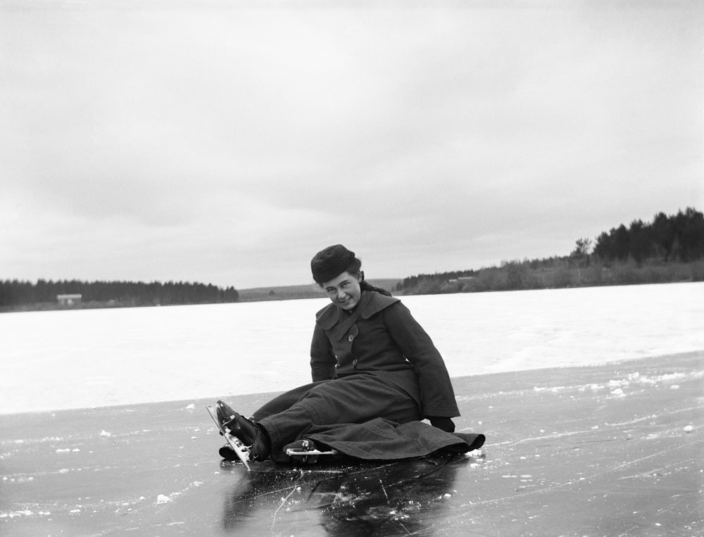 Leende kvinna med skridskor sitter på isen.