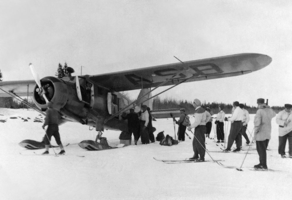 Vinterbild av flygplan på isen, intill står män på skidor.