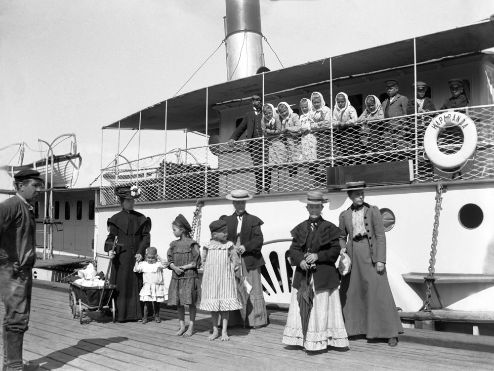 Passagerarbåt intill brygga. Framför och på båten står kvinnor i långa klänningar.