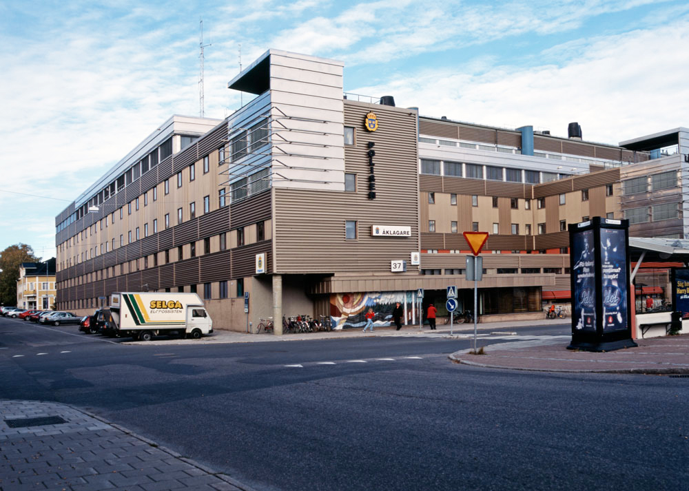 Bild av modern jättestor byggnad med Polisens skylt och brunaktig fasadbeklädnad.