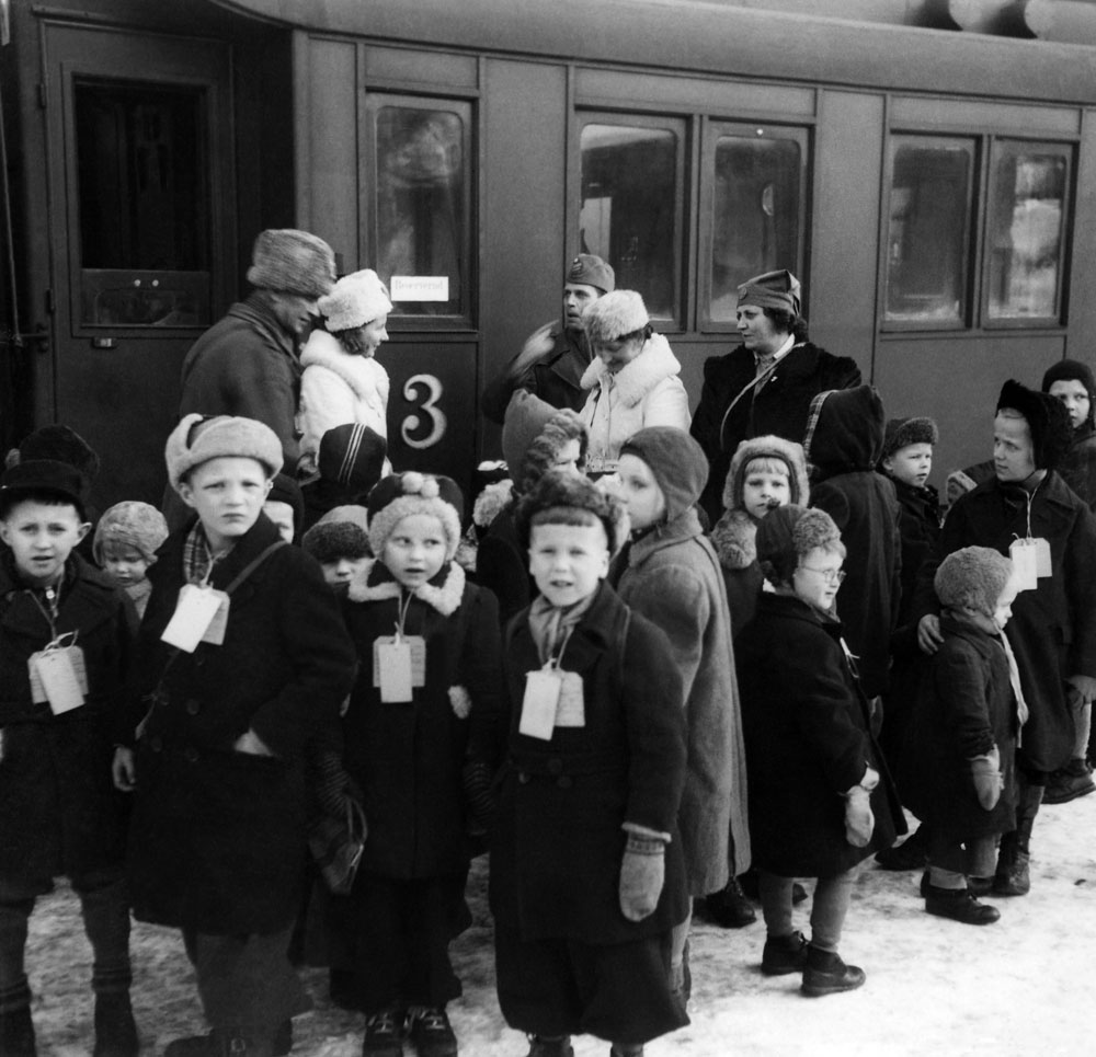 Finska flyktingbarn i vinterkläder framför järnvägsvagn.
