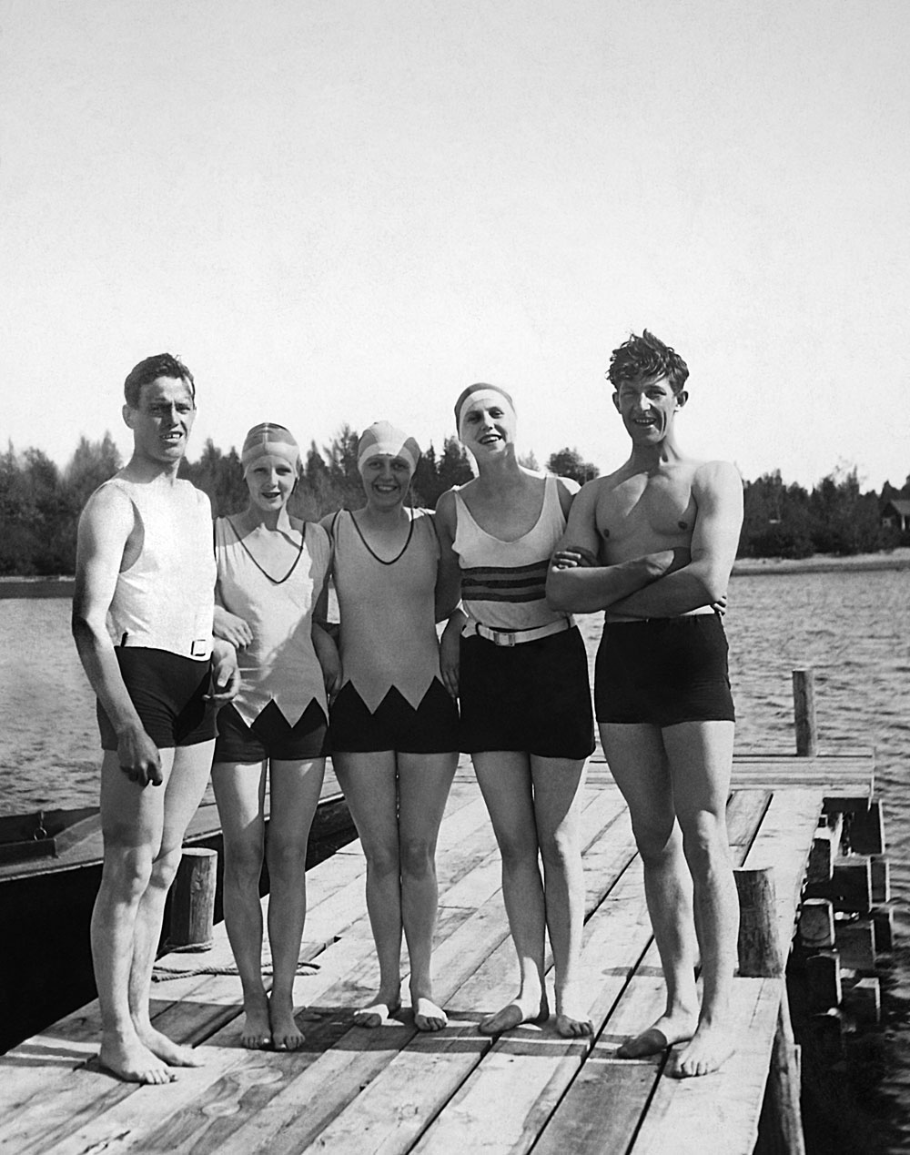 Två unga män och tre kvinnor i badkläder stående på brygga.