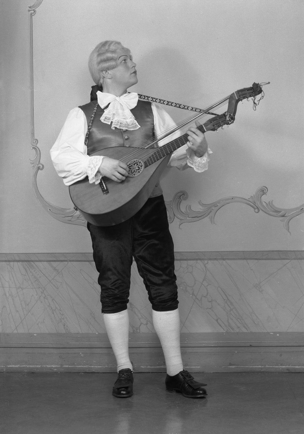 Ingvar Wixell stående i 1700-talsdräkt med vit peruk och luta.