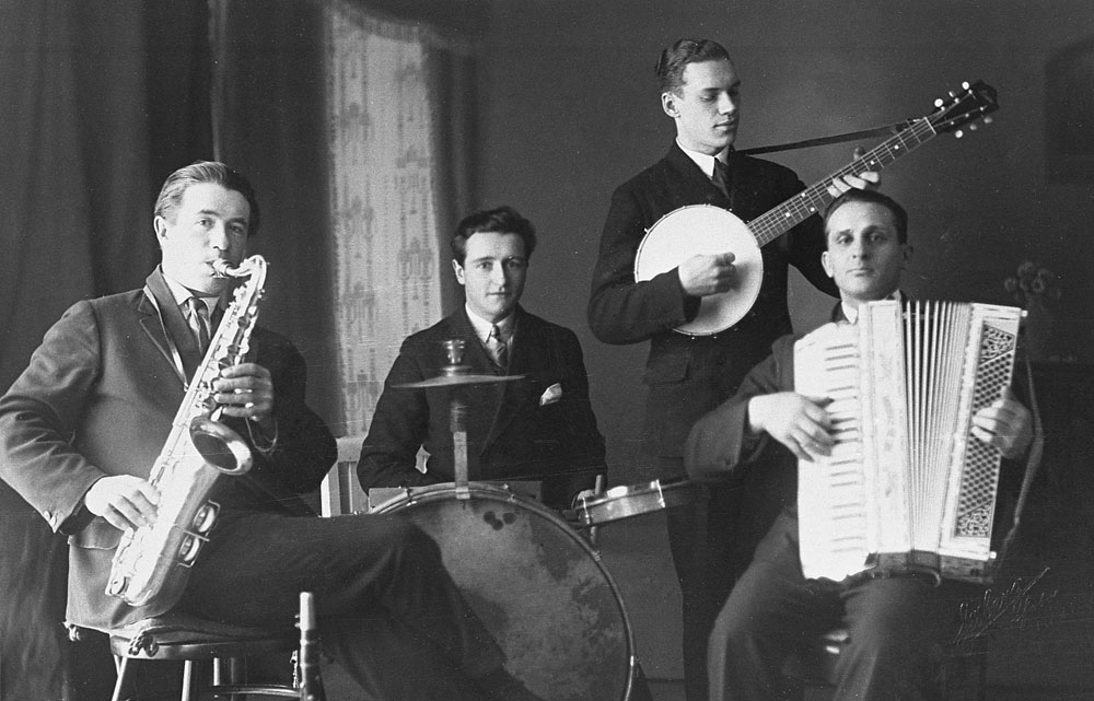 Orkester med fyra män som spelar saxofon, trummor, banjo och dragspel.