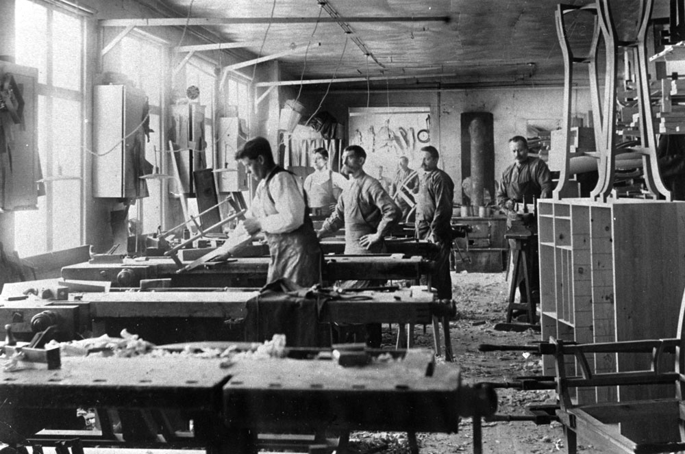 Interiör från möbelfabrik med snickarbänkar och flera arbetande män.