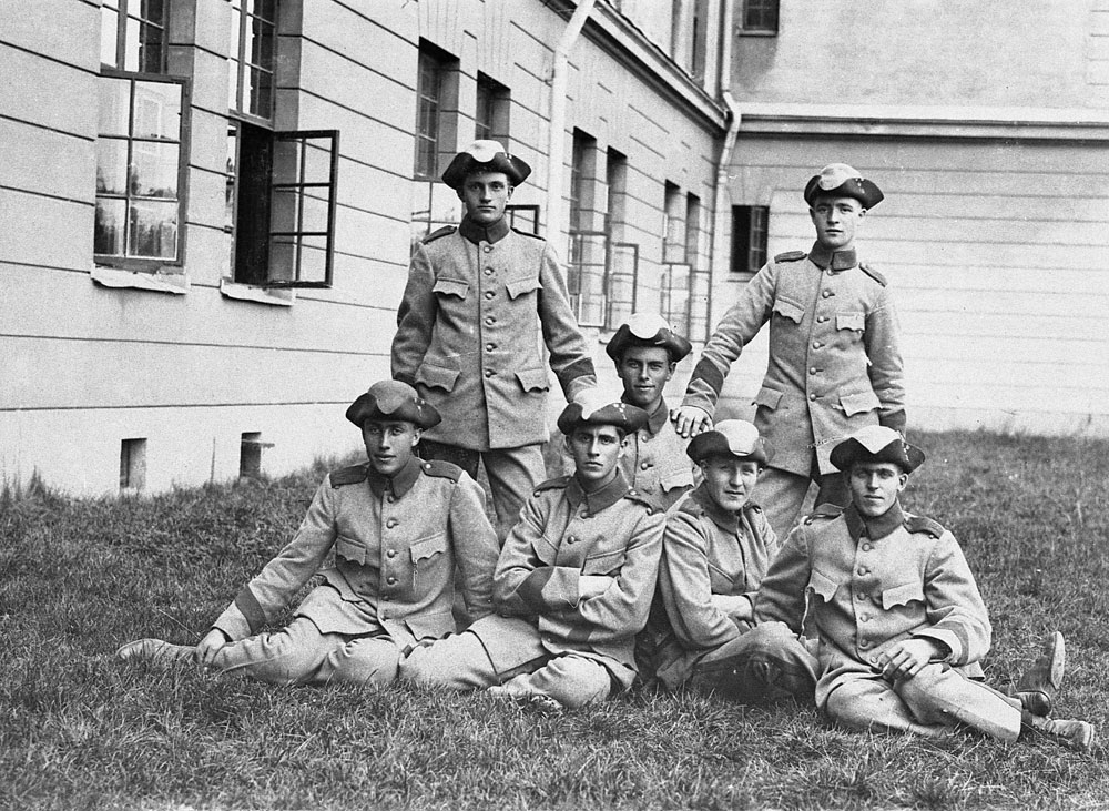 Gruppbild av soldater i uniform vid kasernbyggnad.
