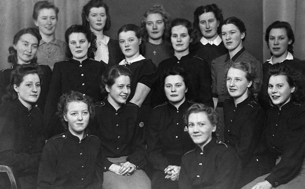Gruppbild med flera unga kvinnor i uniformsliknande mörka jackor.