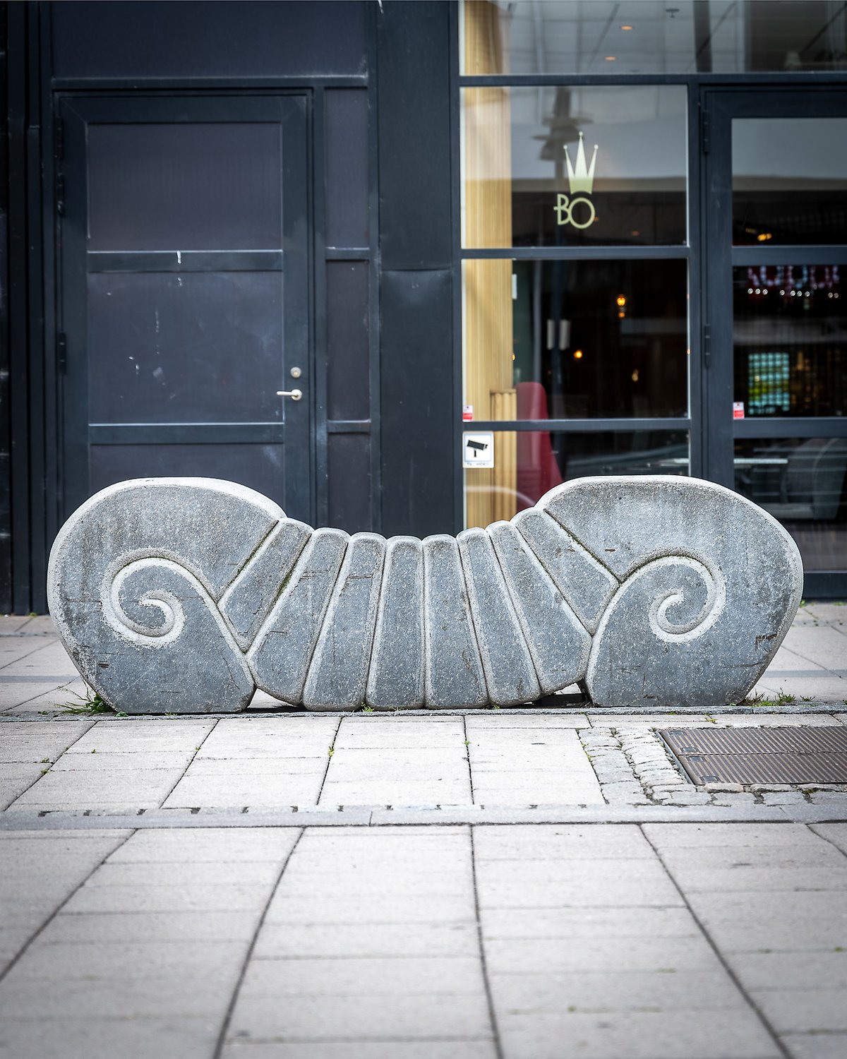 Stenskulpturen Larven i en vybild med omgivande gågata och galleria.