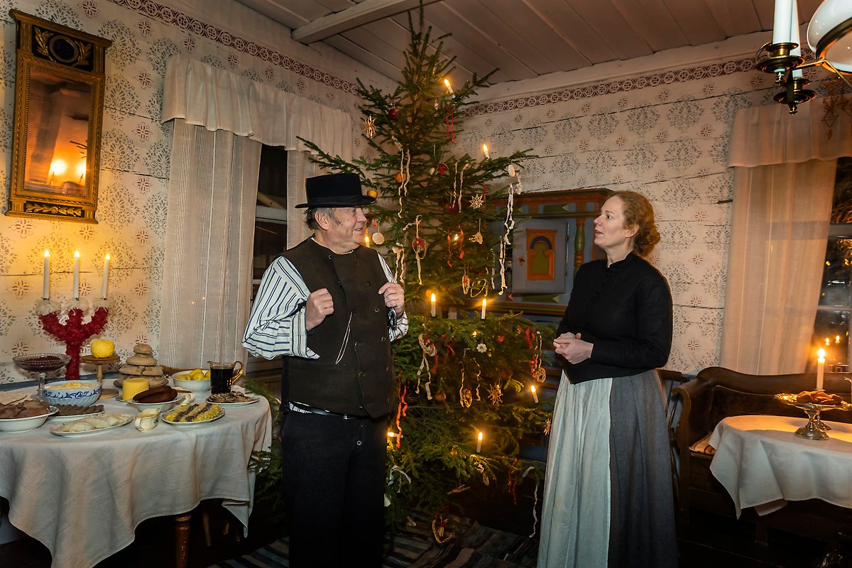 En man och en kvinna klädda i gammeldags kläder inne i ett av husen på Hägnan