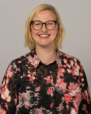 Carina Sammeli ler mot kameran. Hon bär en svartblommig blus och svarta glasögon.