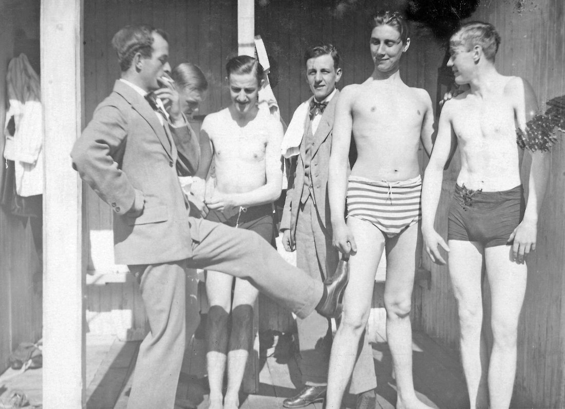 Fem unga glada män, en rökande man i kostym, övrig i badbyxor.
